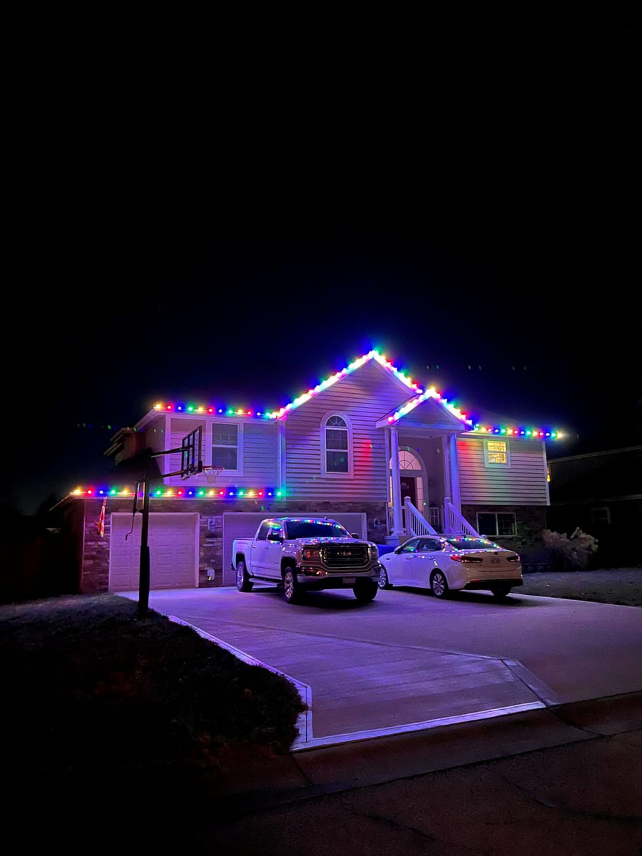 A home's roofline and driveway lined with colorful Christmas lights at night.