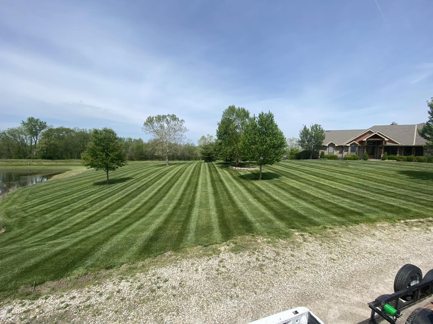 A large acreage lawn mowed in even stripes, curving around a pond and mature trees.