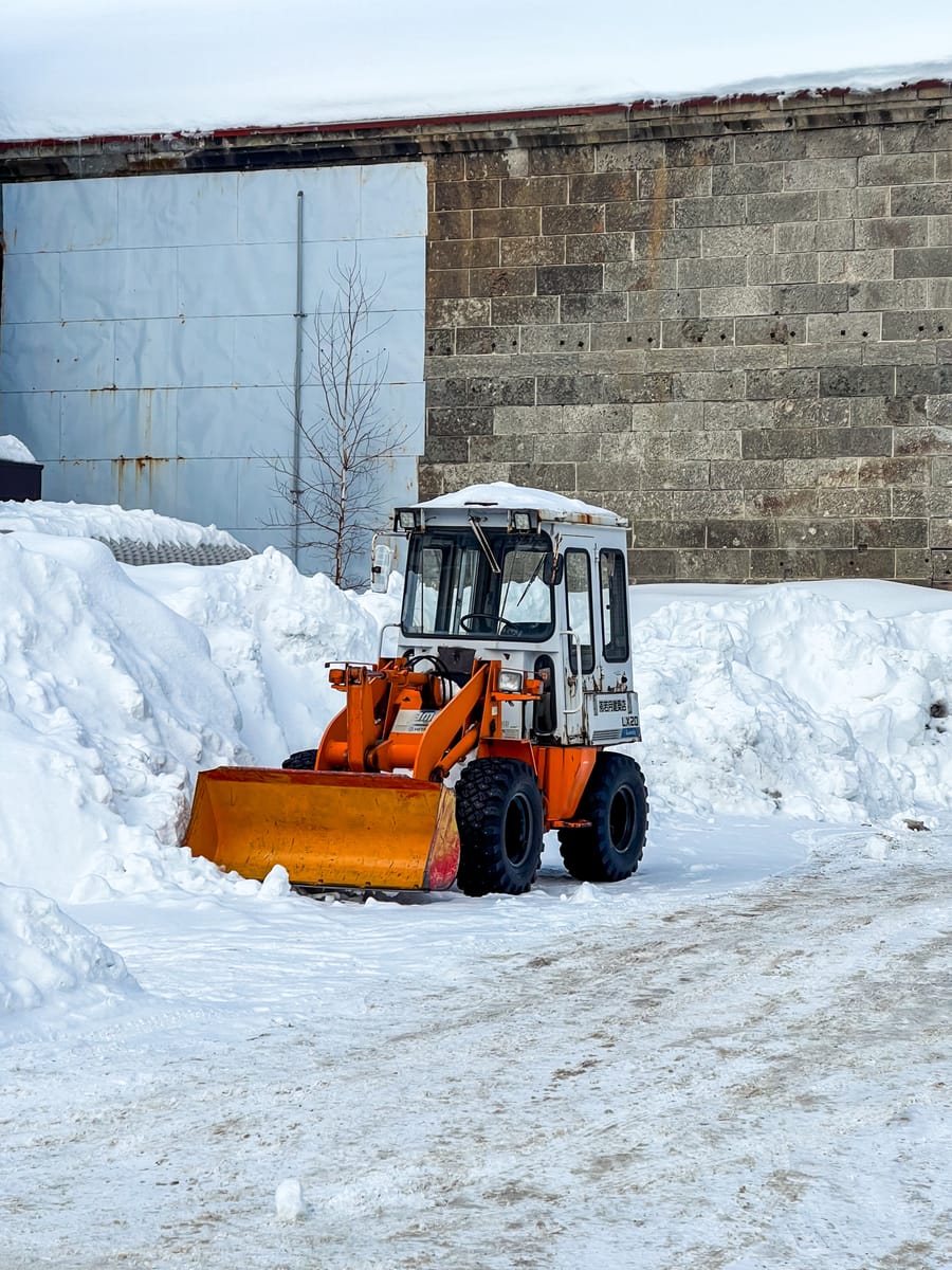 A wheel loader with a plow bucket clearing snow beside tall snow banks.